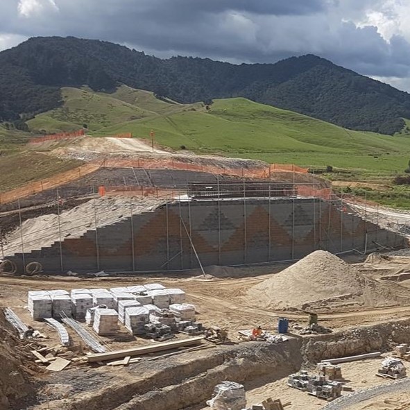 Mechanically stabilized earth (MSE) wall under construction for road embankment with visible block facing and soil reinforcement.