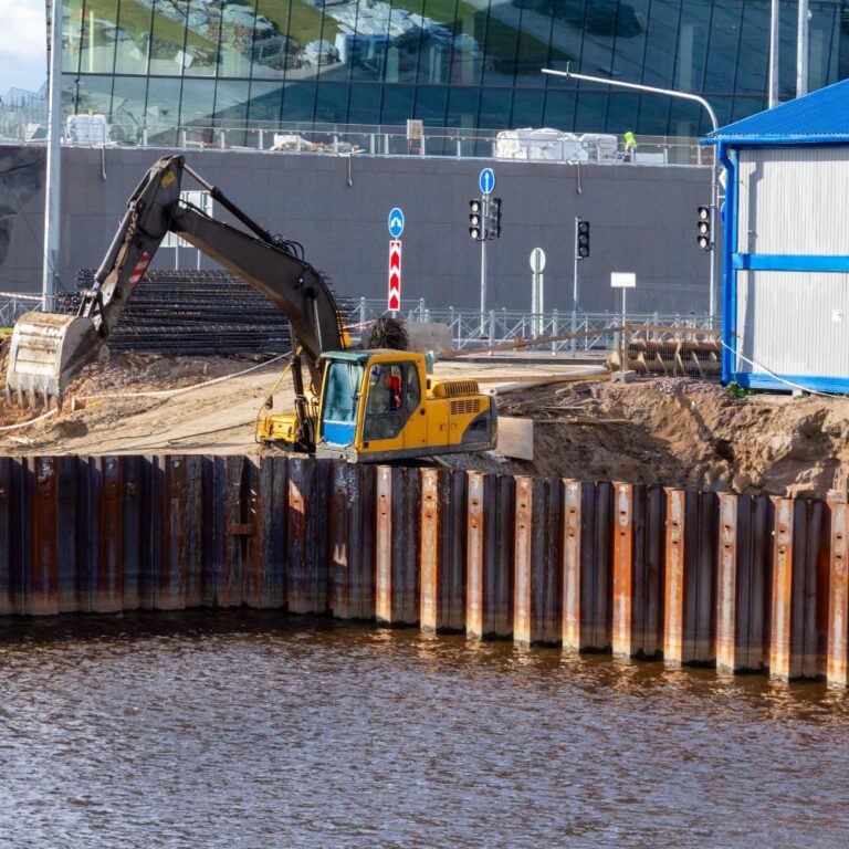 Excavator working behind steel sheet pile wall along a waterfront construction site